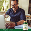 Middle-aged man smiles as he types on a laptop, holding coffee next to a Bacopa bottle.