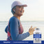 An older woman jogs on a beach carrying a bottle of Calcium Magnesium Citrate plus D3.