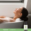 A young woman enjoys a bubble bath, accompanied by a Chamomile Oil bottle nearby.