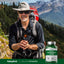 A smiling man in hiking gear holds trekking poles next to a Chelated Potassium 99 mg bottle.