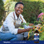 Young adult woman smiling while tending to pepper plants, with a bottle of Norwegian Cod Liver Oil nearby.