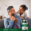 An adult couple smiling while embracing on a couch with a bottle of Graviola (Soursop).