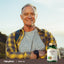 An older man with a smile, arms crossed, stands beside a bottle of Hemp Oil.