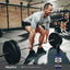 A middle-aged man performs a deadlift in a gym next to an IGF-1+ Liposomal Spray bottle.