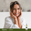 Smiling young woman in a white bathrobe holding a bottle of Jojoba Oil.