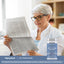 An elderly woman reads a newspaper next to a bottle of Eye Vision Guard.