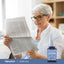 An older woman reads a newspaper next to a bottle of Lutein with Zeaxanthin.