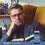 A man with grey hair and glasses is reading a book next to a Lutein + Zeaxanthin supplement bottle.