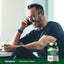 A middle-aged man using a phone and stylus next to a Magnesium Taurate bottle.