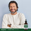 A middle-aged man smiling with arms crossed stands next to a Nascent Iodine bottle.