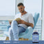 A young man reading a book in a blue armchair next to a bottle of Lutein 20MG with Zeaxanthin.