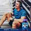 Young adult male in workout clothes sits on stairs, smiling, with a Mega Multi for Men bottle in the foreground.