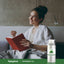 A young woman reads a book on a couch with a Peppermint Oil bottle beside her.