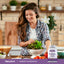 A young woman in a kitchen prepares a salad with fresh lettuce, next to a bottle of Probiotic Acidophilus.