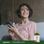 Young woman smiling and holding a smartphone next to a Red Raspberry Leaves supplement bottle.