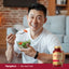 Asian man smiling while holding a salad bowl and fork, with a Red Yeast Rice bottle nearby.
