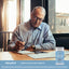 Senior man writing in a notebook with a Senior Vision Care Complex bottle nearby.