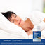 A middle-aged woman sleeps in bed next to a Sleep Formula bottle.
