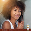 A young woman with curly hair brushes it next to a bottle of Sweet Almond Oil.