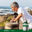 Senior man leaning on a railing by the ocean with a Tinnitus supplement bottle nearby.