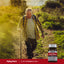 An elderly man hikes with a walking stick next to an Ultra Vitamin K-2 MK-7 supplement bottle.