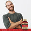 A smiling man with crossed arms stands next to an Ultra Max Advanced Antioxidant bottle, showcasing a lifestyle choice.