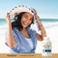 A young woman smiling on the beach holding a Pancreatin Enzyme bottle.