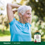An older woman smiling and stretching outdoors with a bottle of Tart Cherry extract.
