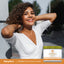 Young adult woman smiles with hands behind her head outdoors, next to a Vitamin C Antioxidant Cream jar.