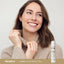 A young woman smiling, holding her sweater collar, with a Vitamin E Moisturizing Stick beside her.