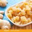 Crystallized ginger in a white bowl on a wooden surface, surrounded by raw ginger roots and a blue mat.